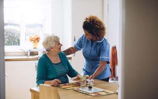caregiver serving a meal to smiling elderly woman in kitchen